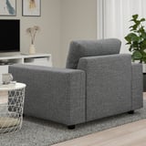 A cozy gray armchair in a living room, accompanied by a side table with a mug and a plant.