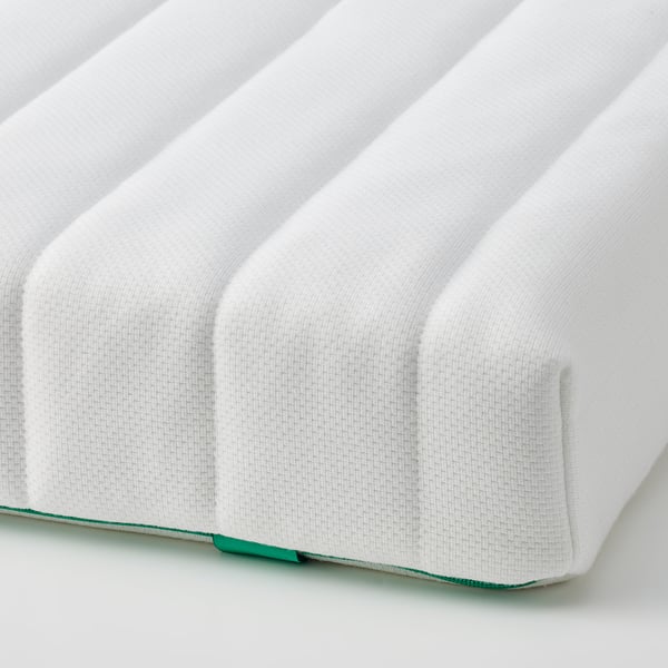 Close-up of a white, cushioned mattress showing its soft, ribbed texture. The stitching and zipper suggest a high-quality, child-safe design.