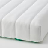 Close-up of a white, cushioned mattress showing its soft, ribbed texture. The stitching and zipper suggest a high-quality, child-safe design.
