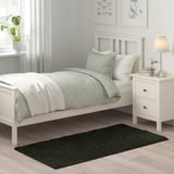 Minimalist bedroom: white bed, green rug, nightstand, lamp, plant. VINDEBÄK rug fits.
