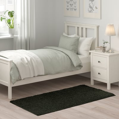 Minimalist bedroom: white bed, green rug, nightstand, lamp, plant. VINDEBÄK rug fits.