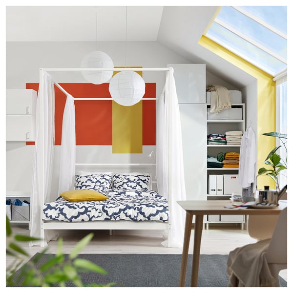 Modern bedroom with colorful VITARNA bed, yellow cushions, white curtains, and plant.