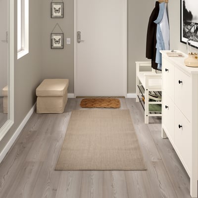 A clean entryway with a VODSKOV rug in beige, blending jute and sisal, placed centrally on light floors, smaller than the dresser beside it.