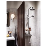Modern bathroom with chrome shower, radiator, concrete walls, white sink counter, toiletries, and round wall light.