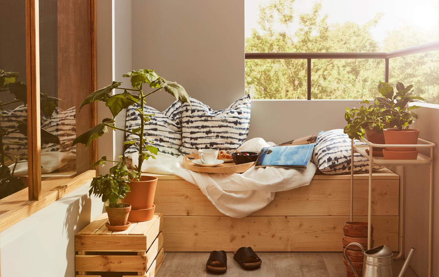 มุมระเบียงและพื้นไม้ยกสูง วางหมอนอิง เครื่องนอน และถาดพร้อมอาหารเช้าชุดเล็ก