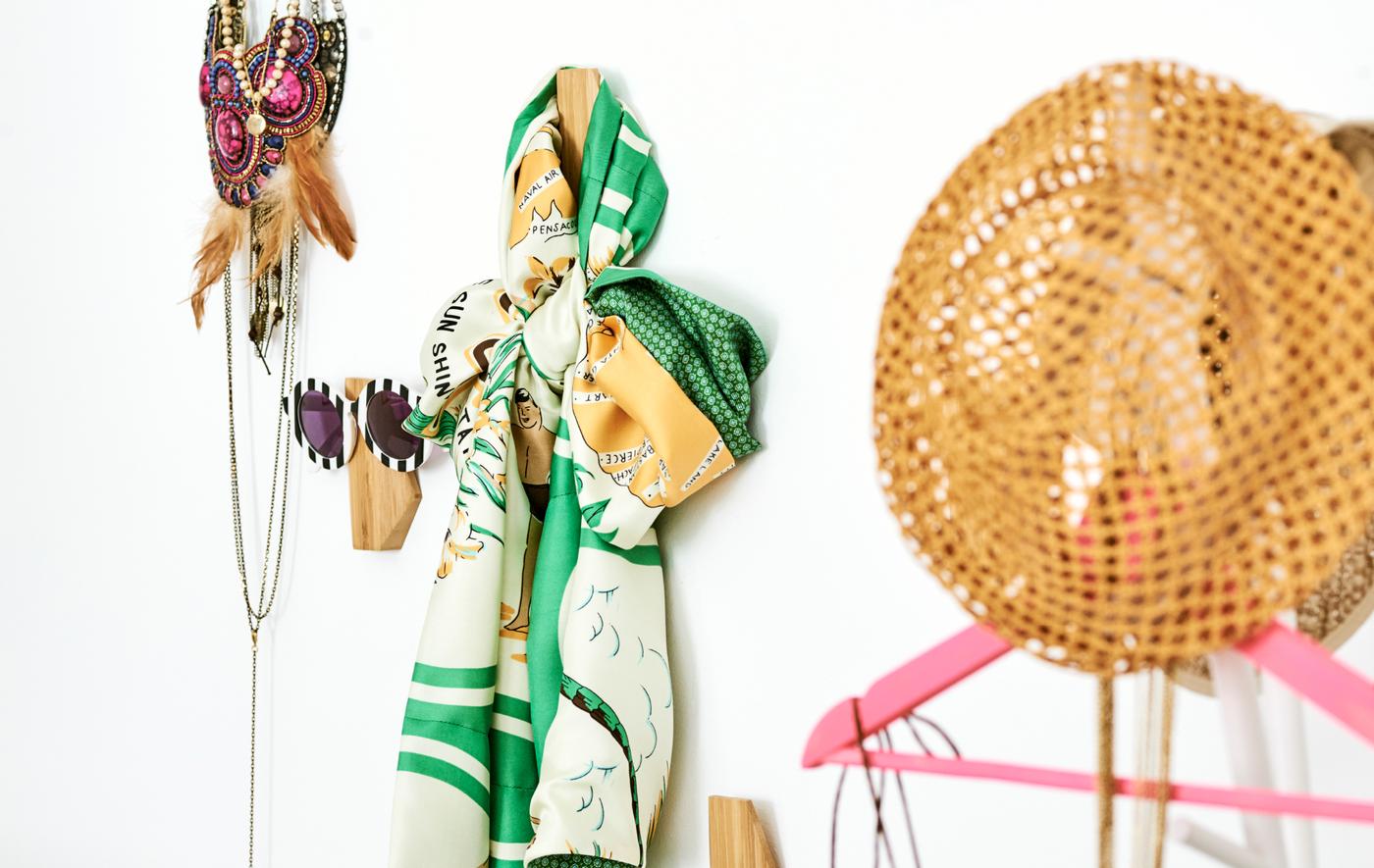 ตะขอไม้ไผ่ติดที่ผนังเรียงแบบอิสระ ตะขอแต่ละตัวแขวนของแต่งตัว อย่างแว่นกันแดด ผ้าพันคอ สร้อยคอ และหมวกฟาง