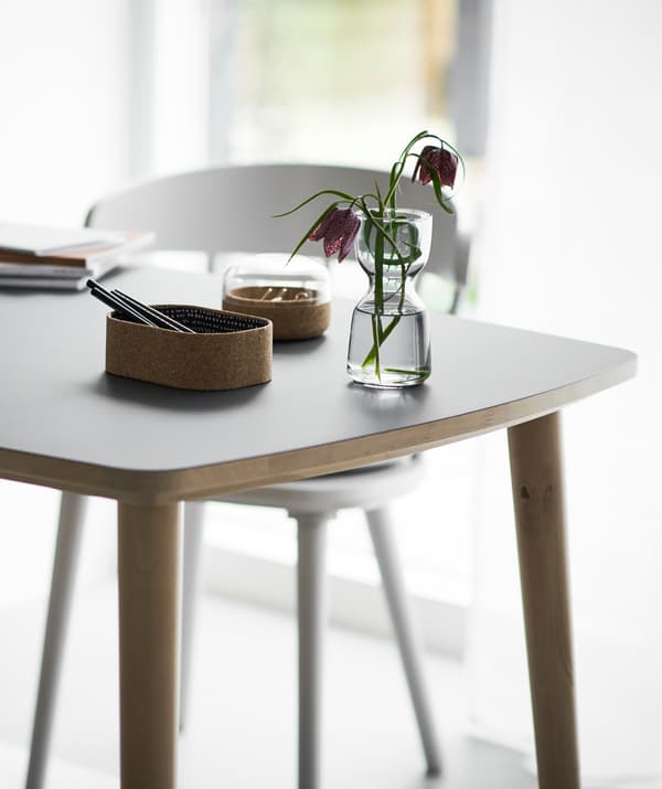 เครื่องเขียนและแจกันดอกไม้อยู่บนโต๊ะที่มีเก้าอี้สีขาว