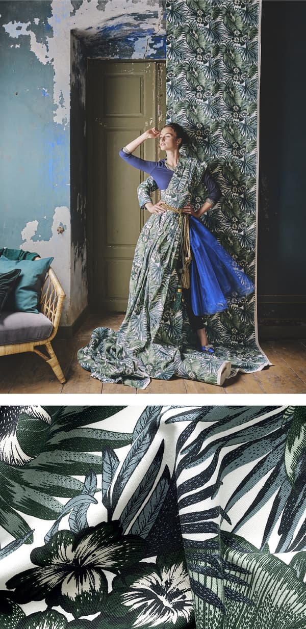 หญิงคนหนึ่งกำลังโพสโดยแต่งกายด้วยผ้าพิมพ์ลายพฤกษาที่มีแขวนไว้บนผนังเช่นกัน