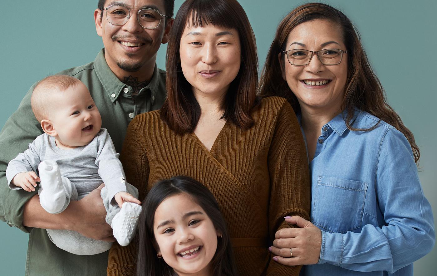 ครอบครัวที่มีสมาชิกห้าคน ทุกคนยิ้ม ตั้งแต่คู่สามีภรรยาและลูกที่ยังเล็ก ลูกสาวที่กำลังโต และคุณยายยืนอยู่ใกล้ ๆ