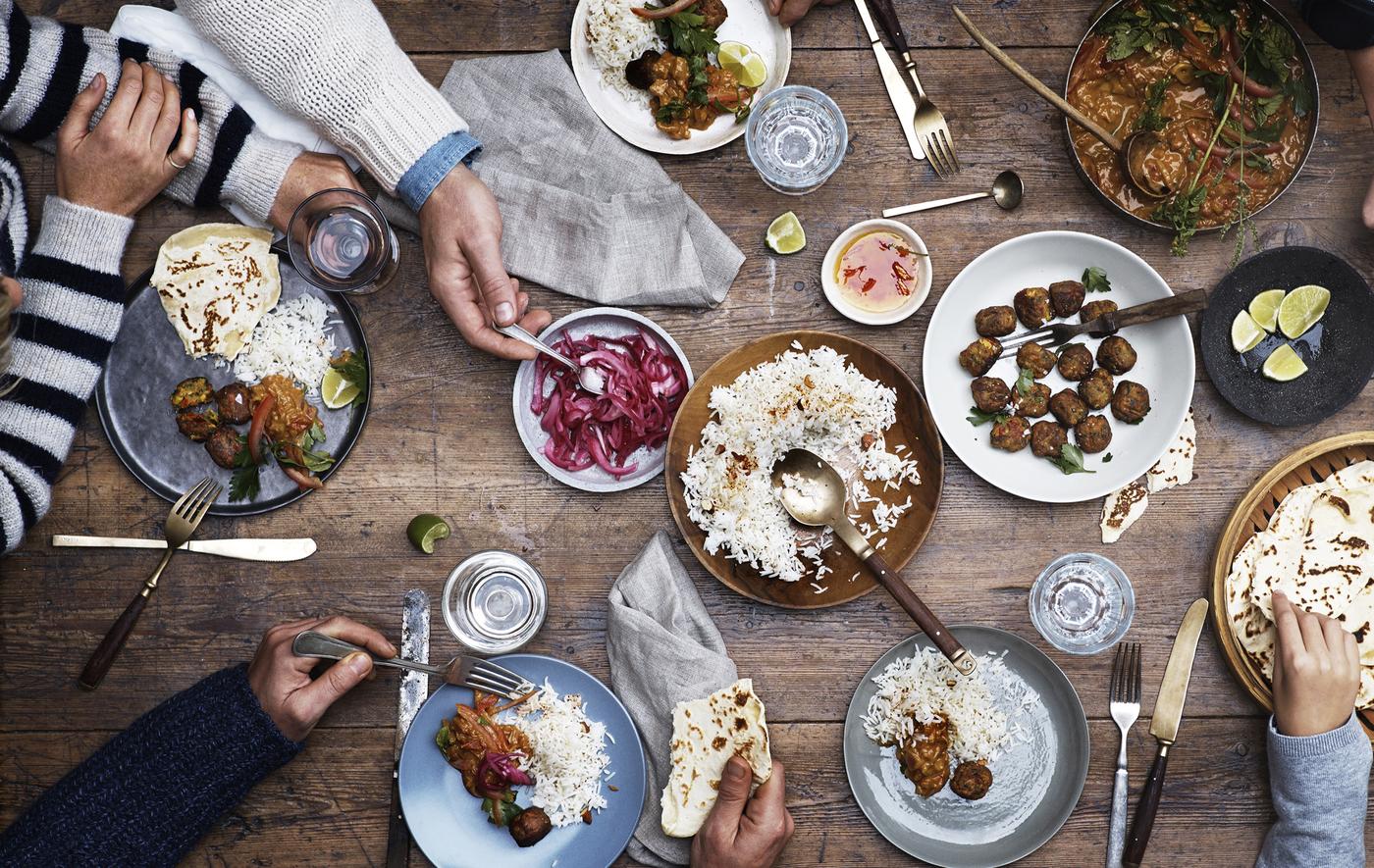 การจัดโต๊ะอาหารที่มีมีทบอล ข้าว และของดองวางอยู่บนโต๊ะไม้พร้อมอุปกรณ์รับประทานอาหาร และการเสิร์ฟด้วยมือ