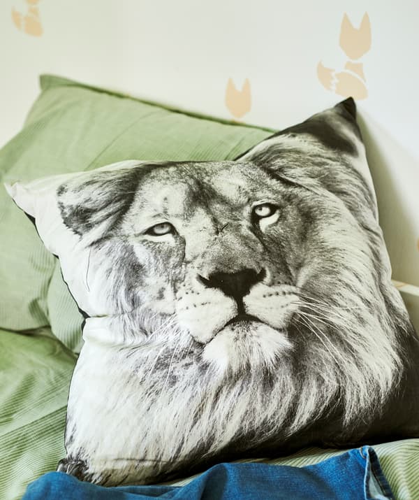 หมอนอิงลายรูปถ่ายสิงโตสีขาวดำบนเตียงที่ปูผ้าปูที่นอนสีเขียว มีผนังพิมพ์ลายรูปสุนัขจิ้งจอกเป็นพื้นหลัง