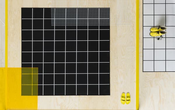 พรมสีดำที่มีเส้นสีขาวและพรมสีขาวที่มีเส้นสีดำบนพื้นไม้สีอ่อน และรองเท้าสีเหลือง