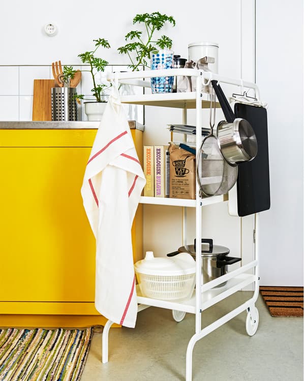 รถเข็นสองล้อเก็บอุปกรณ์ครัวหลายอย่างตั้งอยู่ข้าง ๆ ครัวขนาดเล็กเพื่อวางของเพิ่มเติม