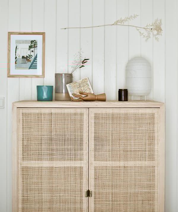 ตู้ไม้เก็บของทรงสูงที่มีบานตู้แบบสานวางติดกับแผ่นผนัง บนหลังตู้มีโคมกระดาษกับของตกแต่ง