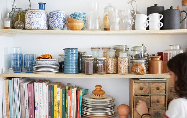 เครื่องครัว หนังสือ และโถใส่วัตถุดิบแห้งบนชั้นวางของสามชั้นที่ทำด้วยไม้