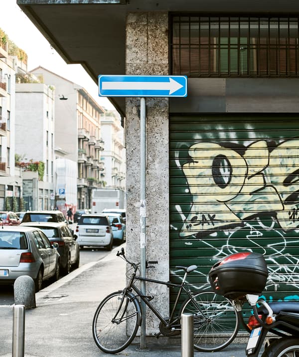 ถนนในเมืองที่มีรถยนต์จอดอยู่ และจักรยานพิงอยู่กับผนังที่มีงานกราฟิตี้