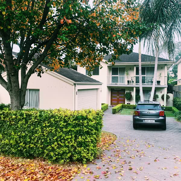 รถสีเทาเข้มจอดอยู่ที่ทางเข้าบ้านของบ้านสีขาวหลังใหญ่ที่มีต้นไม้อยู่โดยรอบ