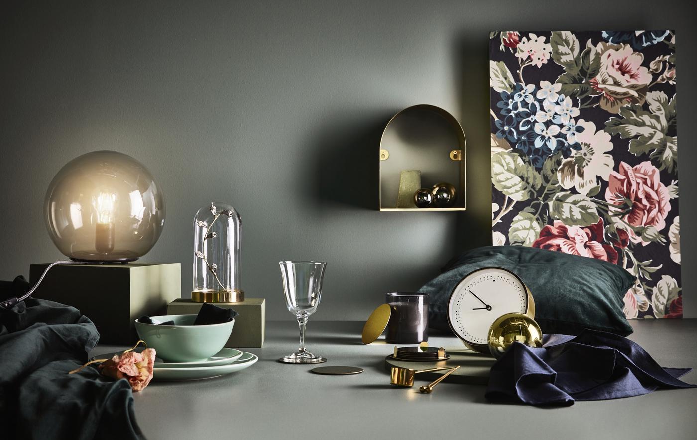 สิ่งของต่างๆ มากมายจัดเรียงบนพื้นที่ใกล้ๆ พื้นหลังสีเข้ม ประกอบด้วยนาฬิกา โคมไฟตั้งโต๊ะและโดมแก้ว