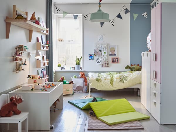 화이트/페일 핑크 옷장, 바닥에 깔린 그린 색상의 놀이매트, 화이트 색상의 놀이테이블과 부드러운 공룡 장난감이 있는 키즈룸.