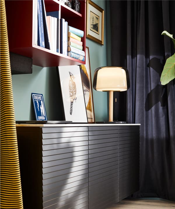 ส่วนของห้องนั่งเล่นที่มีตู้ติดผนังอยู่ระดับต่ำ ตู้หนังสือ ผ้าม่าน โคมไฟและของตกแต่ง สีที่เข้ม