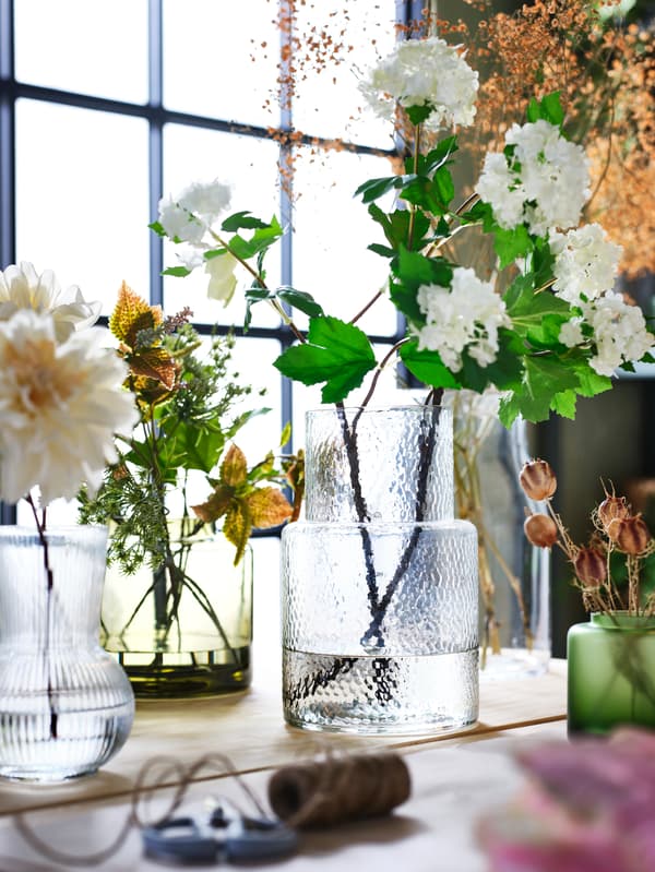 אגרטלים בזכוכית יושבים בחלון עם פרחים לבנים בפנים.