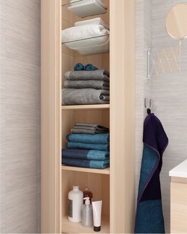 화이트스테인 참나무 베니어 소재의 키큰장이 열려 있고 선반 위로 여분의 수건, 샴푸 등을 위한 넉넉한 수납공간이 보이는 모습