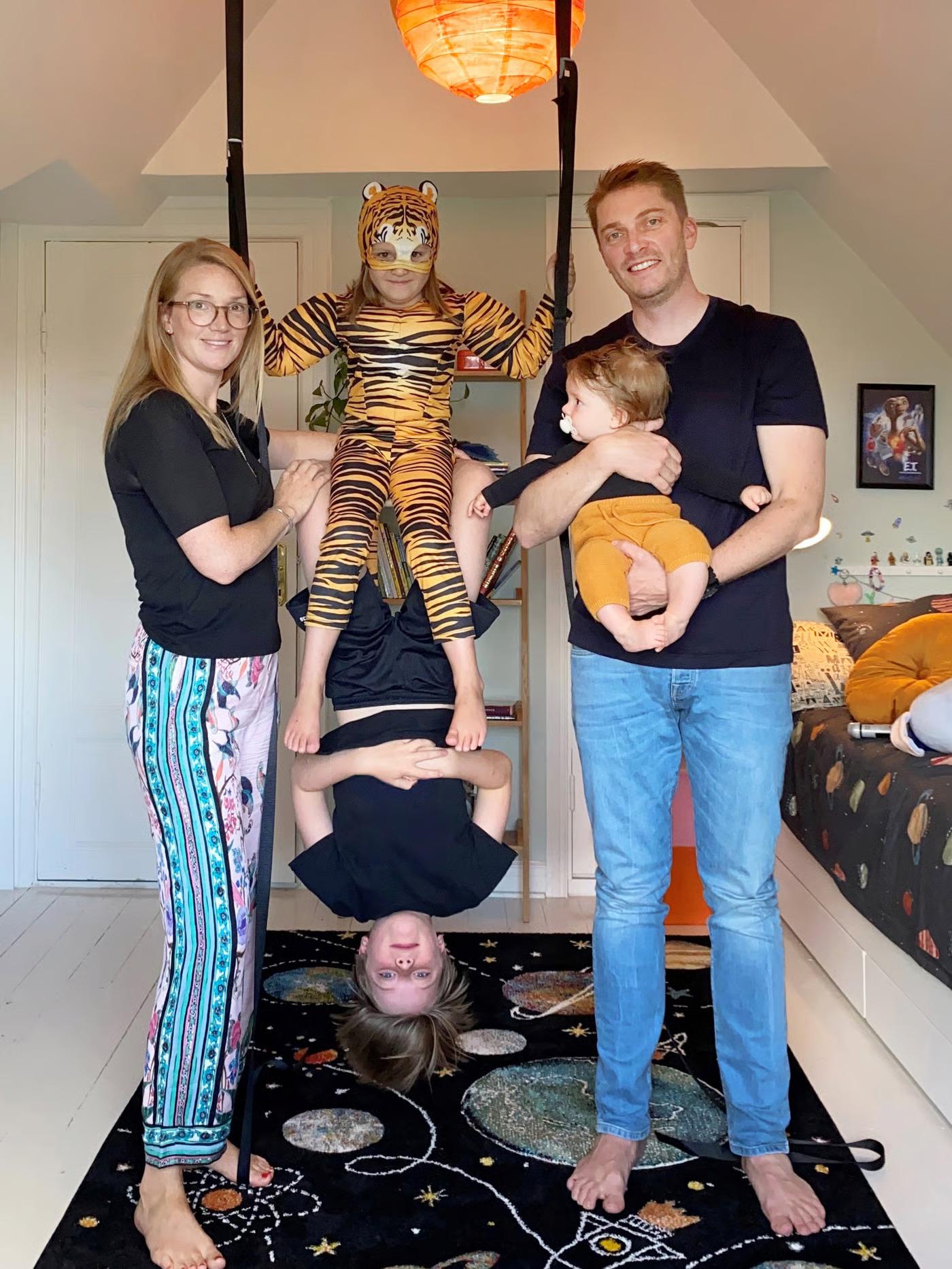 בני משפחה עומדים בחדר ילדים. שני ילדים בתחפושות משחקים על נדנדה שתלויה מהתקרה. האימא מחזיקה את הנדנדה והאבא מחזיק בזרועותיו פעוט.