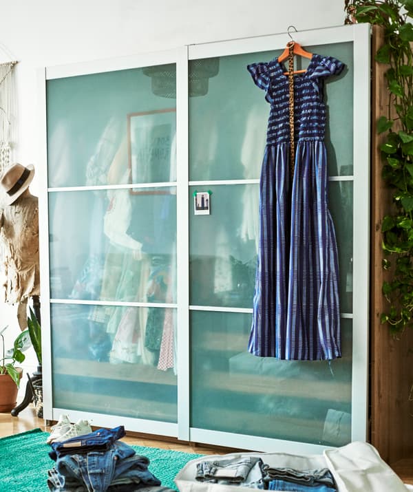 ชุดกระโปรงสีน้ำเงินแขวนอยู่ด้านหน้าตู้เสื้อผ้าบานเลื่อน มีหุ่นลองเสื้ออยู่ข้าง ๆ และกางเกงยีนส์วางอยู่ด้านหน้า