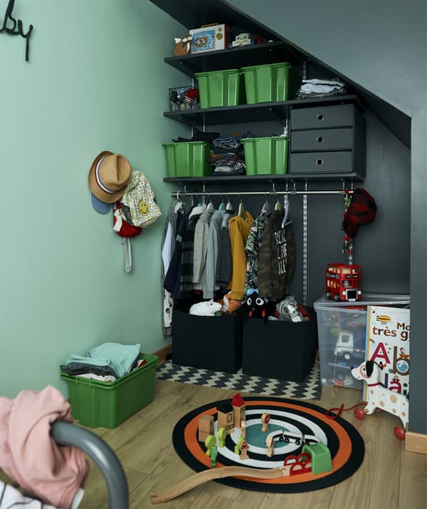 ชั้นวางของ กล่องและราวแขวนเสื้อผ้าติดตั้งไว้ที่มุมที่มีกำแพงสีเขียวในห้องนอนของเด็กๆ