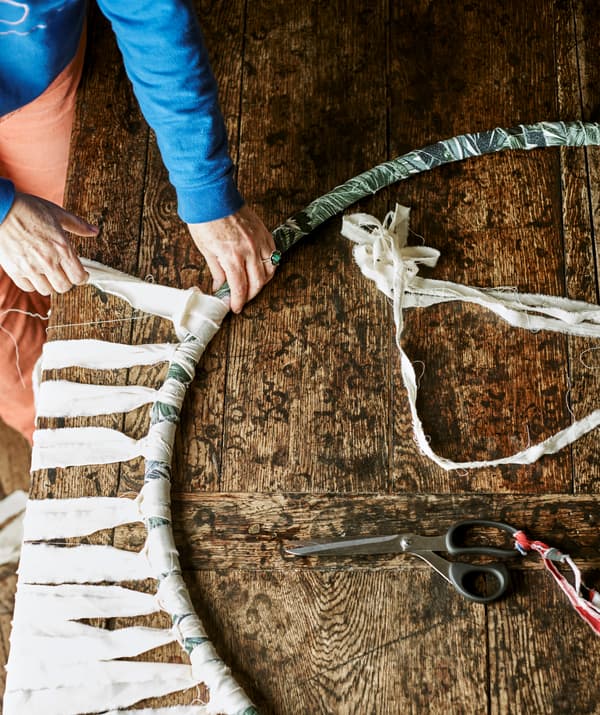 มือกำลังผูกผ้าเป็นเส้นสีเนเชอรัลเพื่อใช้เป็นพู่เส้นของห่วงฮูลาฮุบที่หุ้มด้วยผ้าสีน้ำเงินและสีเขียว