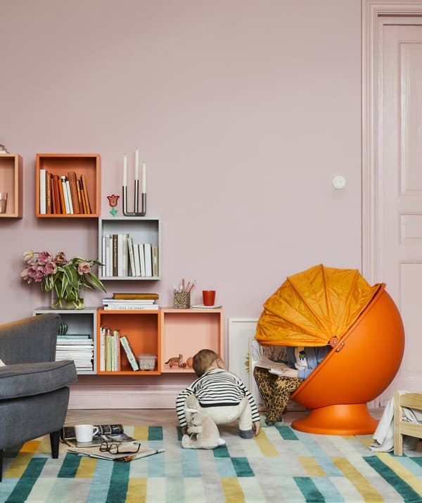 ห้องนั่งเล่นสีสันสดใสกับเก้าอี้รูปไข่สีส้มของเด็กคนหนึ่ง และเด็กสองคนกำลังอ่านหนังสือและเล่น
