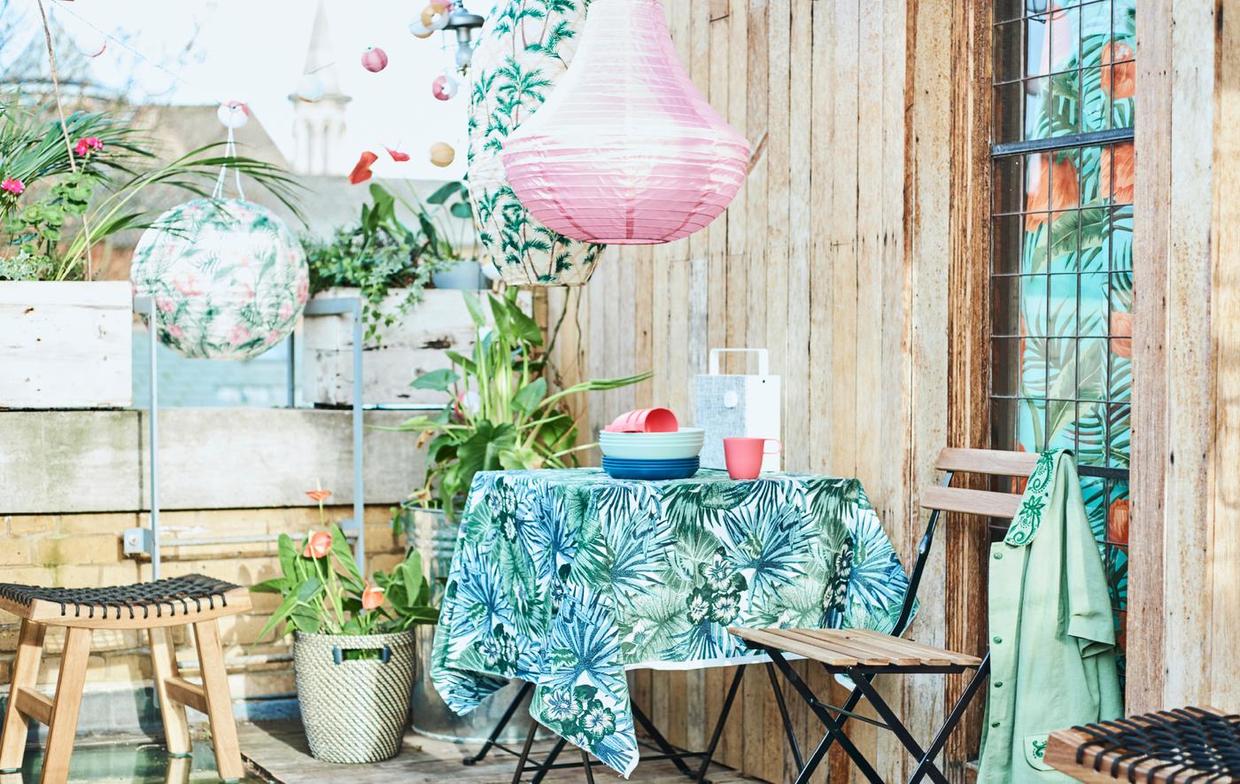 เทอเรซดาดฟ้าวิวเมืองพร้อมโต๊ะลานบ้านปูด้วยผ้าลายใบไม้ เก้าอี้พับ ไม้กระถาง และโคมหลากสี