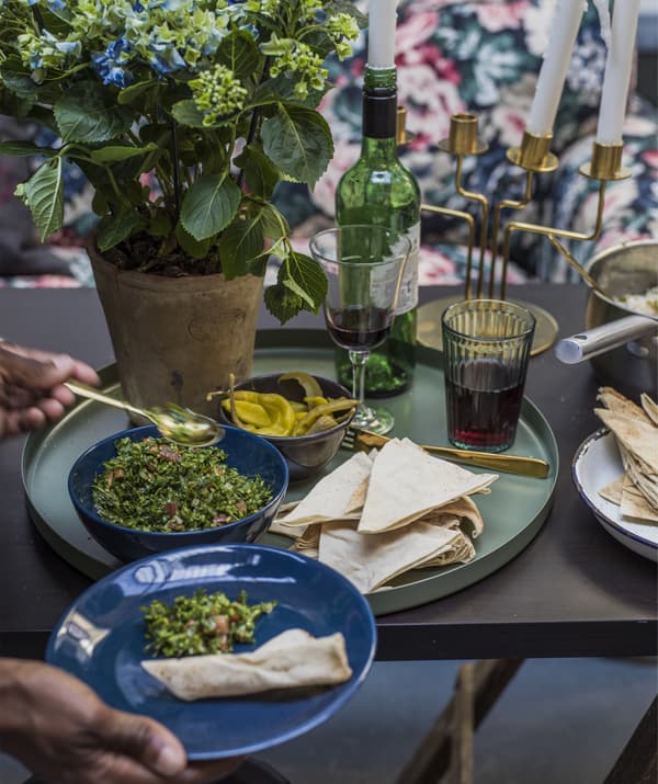 ภาพโคลสอัพของโต๊ะอาหารกับถาดสีเขียวที่มีชามอาหารและมือคู่หนึ่งนำอาหารใส่ลงในจาน