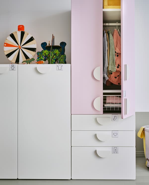 화이트 색상의 인출식 유닛, 화이트 색상의 서랍, 페일 핑크 색상의 도어로 구성된 옷장. 열려 있는 한쪽 도어 사이로 수납된 옷이 보입니다.