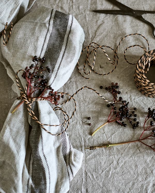 ผ้าเช็ดจานสีธรรมชาติตกแต่งด้วยเชือกพันกิ่งเบอร์รี่นำมาใช้แทนผ้าเช็ดปาก กลุ่มเชือกวางอยู่ด้านข้าง