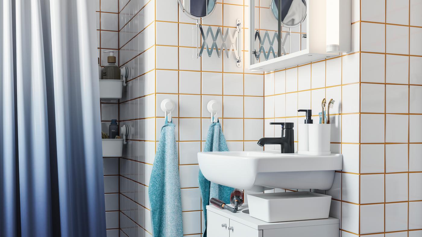 ตู้อ่างล้างหน้าสีขาว ก๊อกน้ำสีดำ กระเบื้องสีขาวพร้อมยาแนวสีเหลือง ผ้าม่านอาบน้ำสีน้ำเงิน และตะขอพร้อมผ้าขนหนู