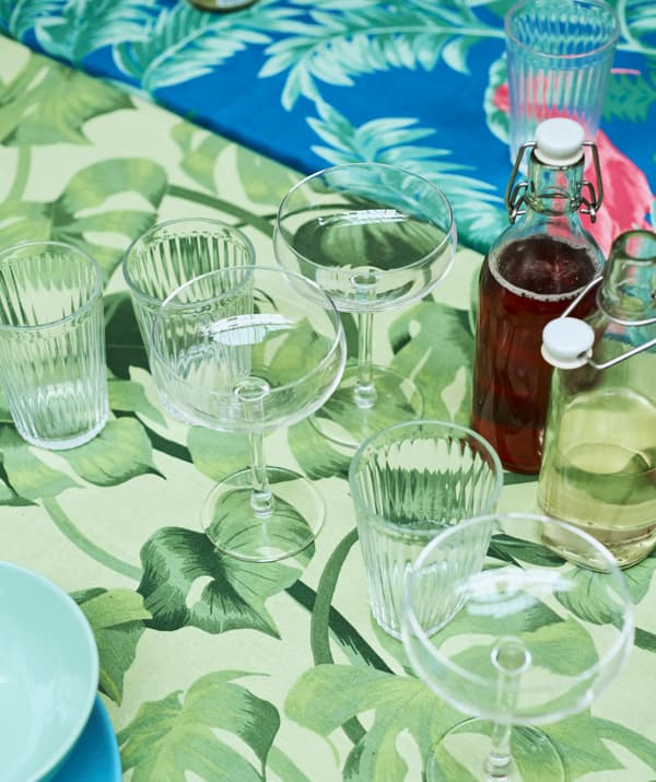 แก้วแชมเปญและแก้วน้ำพร้อมขวดแก้วใส่เครื่องดื่มวางอยู่บนโต๊ะที่ปูด้วยผ้าลายใบไม้สีเขียว