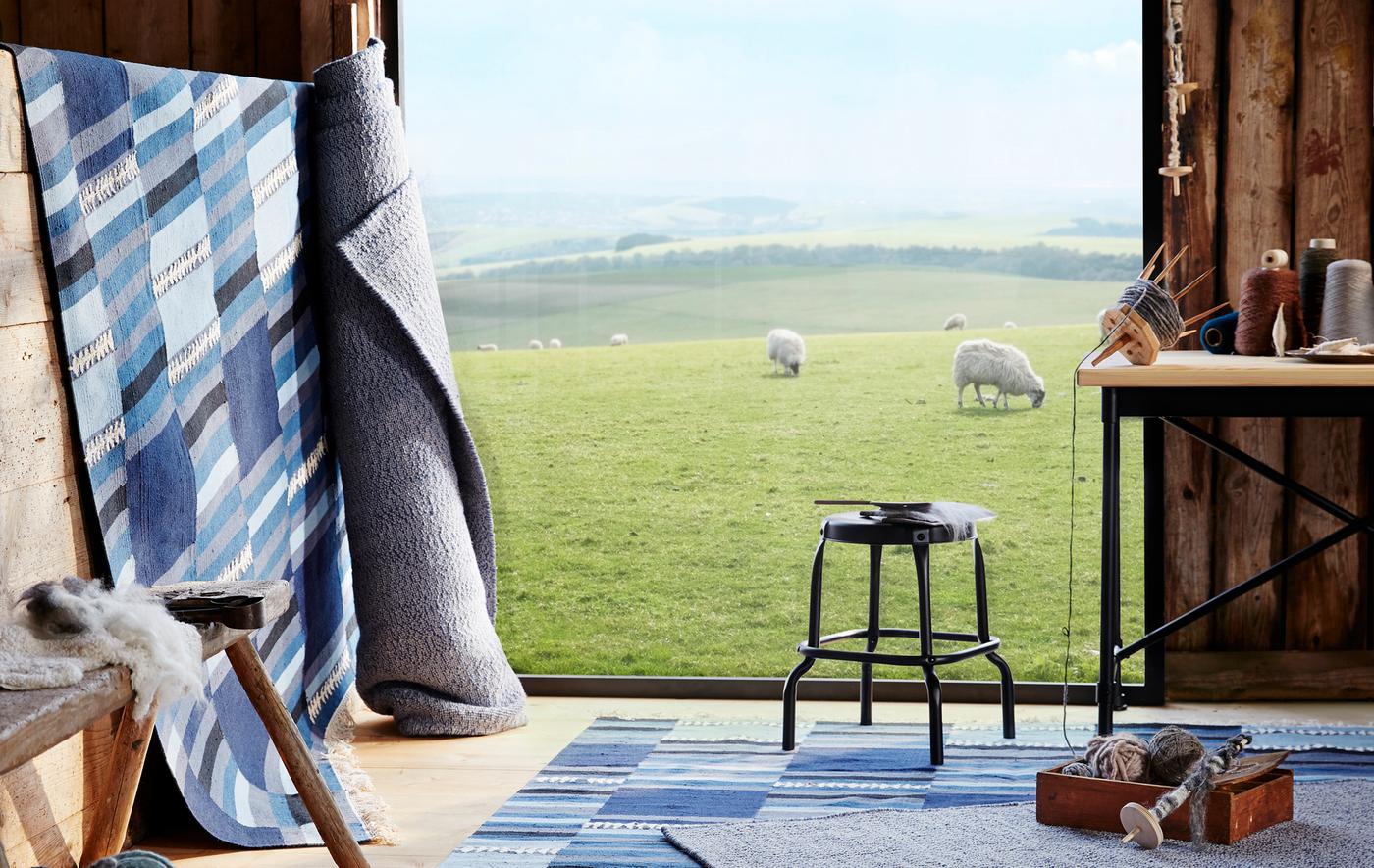 พรมสีน้ำเงินและสีเทาปูอยู่ที่พื้นและม้วนพิงอยู่ที่ห้องที่ทำด้วยไม้ มองออกไปยังทุ่งที่มีแกะ