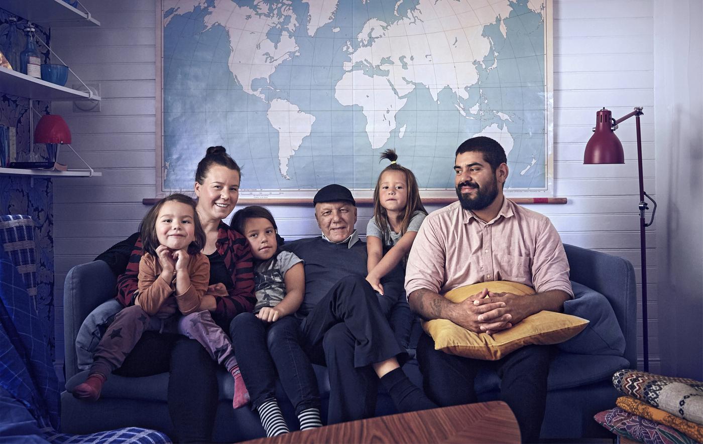 ห้องนั่งเล่นกับครอบครัวที่นั่งบนโซฟาสีน้ำเงิน, แสงไฟ, ชั้นวางของและแผนที่โลกที่อยู่บนผนัง