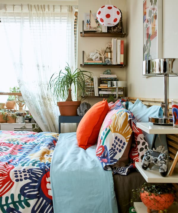 ผ้าสีสดใสบนเตียงที่มีที่เก็บของที่หัวเตียงและชั้นวางติดผนัง