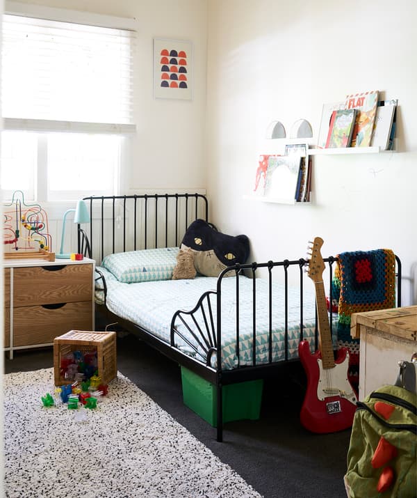 ห้องนอนเด็กมีผนังสีขาว โครงเตียงสีดำ และหนังสืออยู่บนชั้นวางกรอบรูป