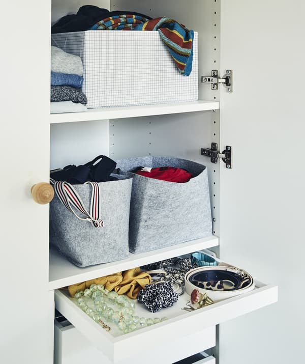 ชั้นวางเสื้อผ้าเต็มไปด้วยตะกร้า กล่อง และเสื้อผ้าที่พับไว้ รวมทั้งลิ้นชักใส่เครื่องประดับอื่นๆ