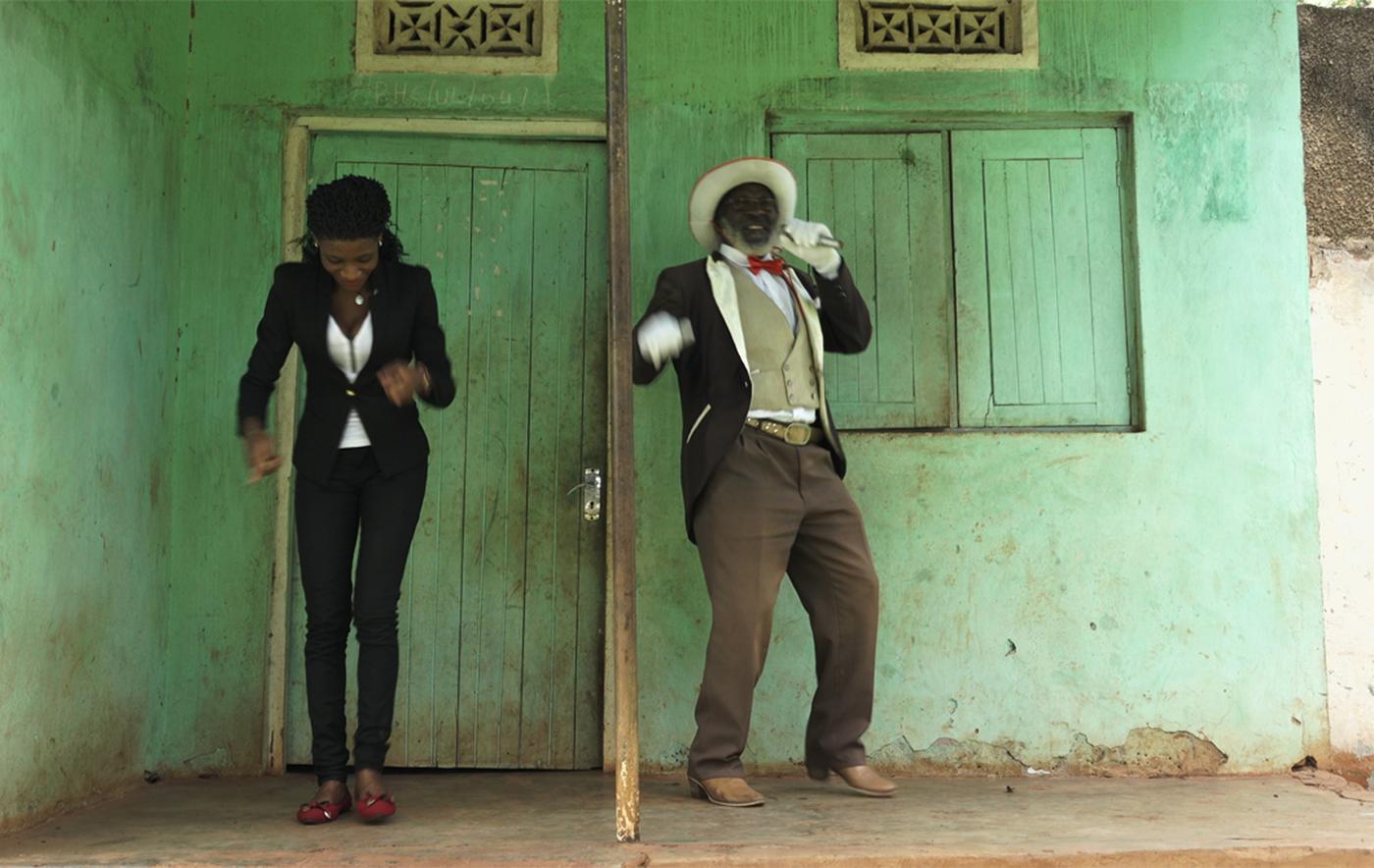 ผู้ชายและผู้หญิงสวมชุดที่ดูสมาร์ทกำลังเต้นอยู่ที่ด้านหน้าอาคารสีเขียว