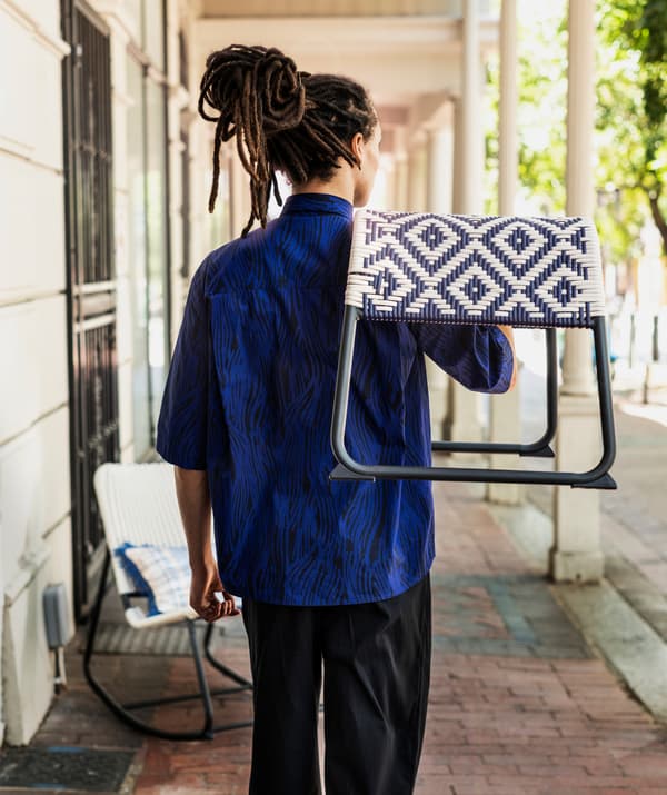 ผู้ชายสวมเสื้อเชิ้ตสีน้ำเงินถือสตูลวางเท้ามีลวดลายสีน้ำเงินและสีขาวไว้บนไหล่ตรงบริเวณกลางแจ้ง