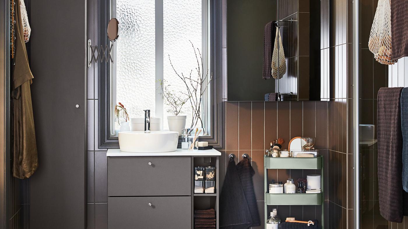 חדר רחצה עם רהיטים בצבע אפור כהה, ארונית עם דלת מראה ועגלת אחסון אפורה-ירוקה.