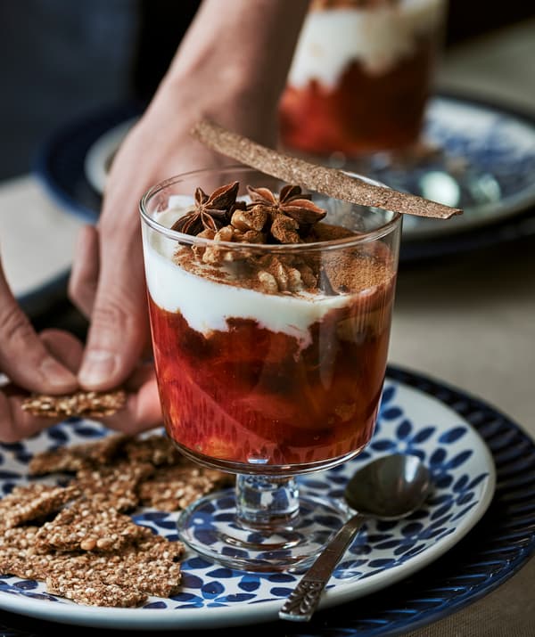 แก้วของหวานมีผลไม้ฤดูหนาวเชื่อมและโยเกิร์ตวางอยู่บนจานลายดอกไม้สีน้ำเงิน