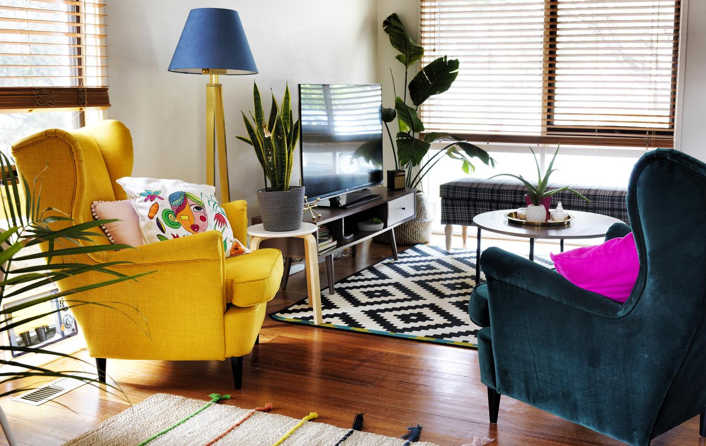 ห้องนั่งเล่นที่มีเก้าอี้วิงแชร์ สีเหลืองและสีเขียวเข้ม พรมสีดำและสีขาว และโทรทัศน์