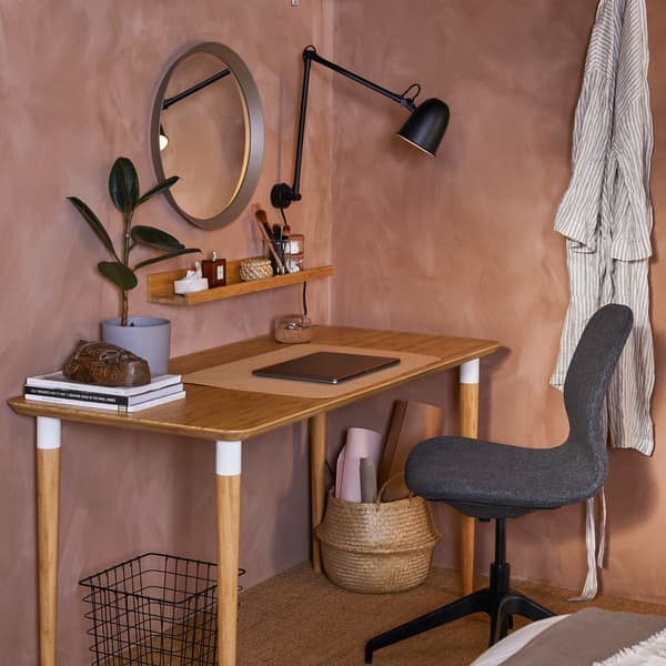 โต๊ะทำงานที่ทำจากไม้ไผ่ซึ่งมีรายละเอียดปลีกย่อยเป็นสีขาว โคมไฟติดผนังสีดำ กระจกเงาทรงกลม และเก้าอี้นั่งประชุมสีเทาเข้ม