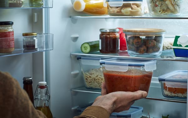 ตู้เย็นที่เปิดอยู่ซึ่งชั้นต่าง ๆ อัดแน่นไปด้วยกล่องบรรจุอาหารสีใส