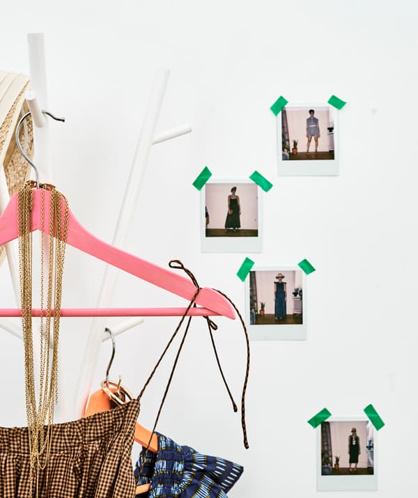 ชุดกระโปรงลายตารางสำหรับซัมเมอร์แขวนอยู่ที่ไม้แขวนสีสดใสบนที่แขวนเสื้อโค้ทตรงผนังที่มีภาพผู้หญิงสวมชุดหลาย ๆ แบบติดอยู่